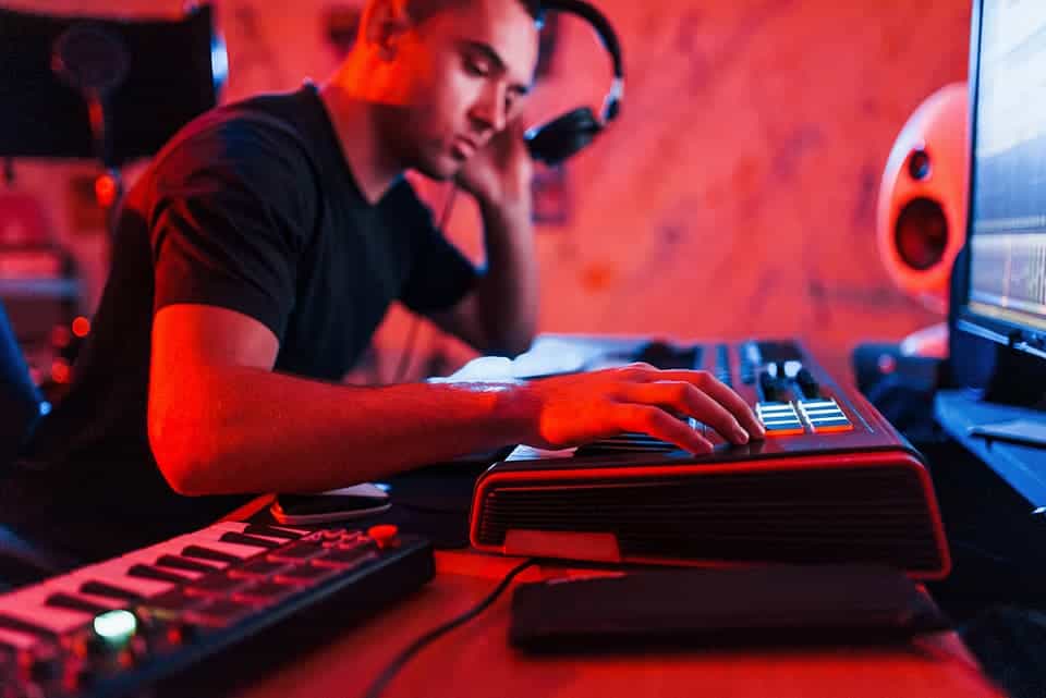 Un futur créateur musical certifié s'immerge dans sa formation sur la musique assistée par ordinateur, ajustant avec assurance les paramètres d'un synthétiseur sous l'écoute attentive de son casque audio.